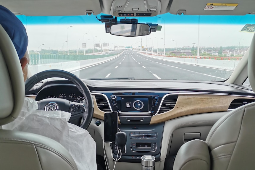 The view of a car's windscreen and the back of the taxi driver's head from the backseat.