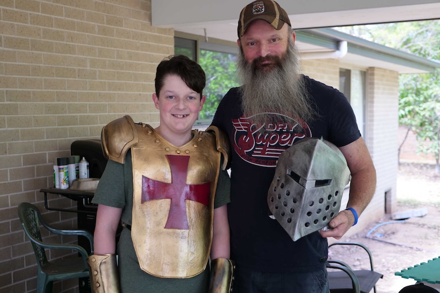 A man stands with his son standing next to him, wearing theatre props, including a gold armour breast plate.