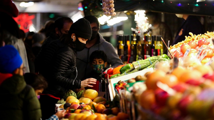 Customers shop for fruit and vegetables at market stalls. 