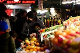 Customers shop for fruit and vegetables at market stalls. 
