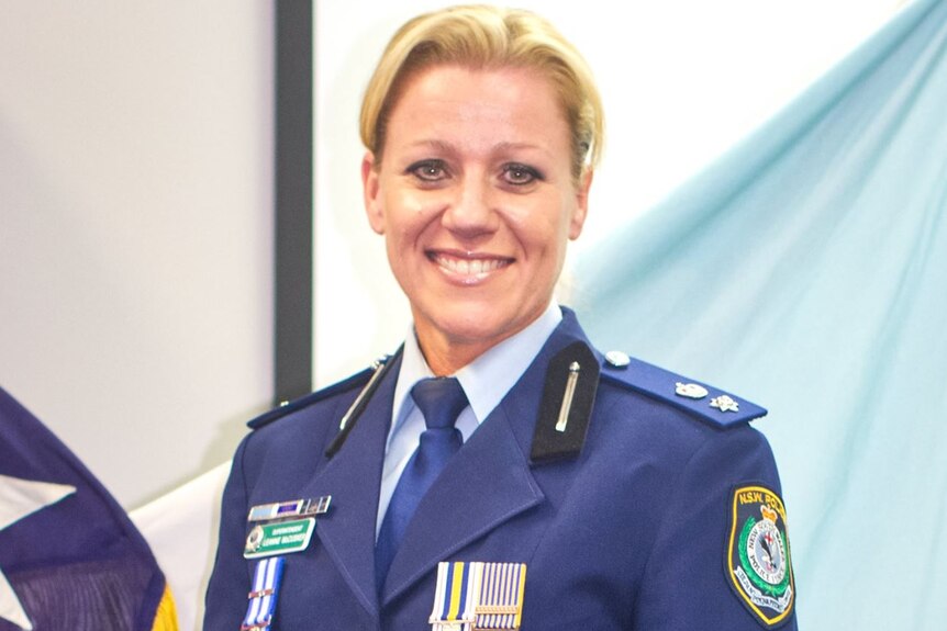 a police woman wearing a dark blue blazer smiling in front of a flag