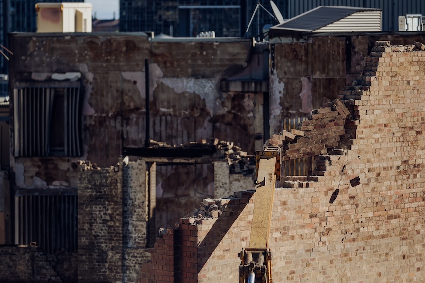 A crane knocking bricks out of a city building wall