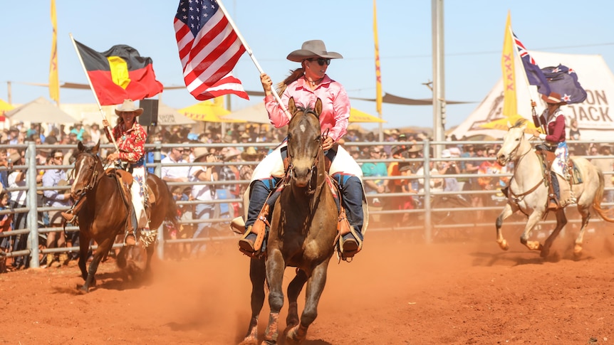 Three women riding horses and carry flags.