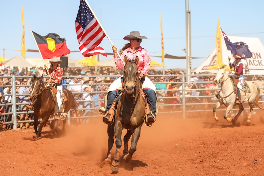Three women riding horses and carry flags. 
