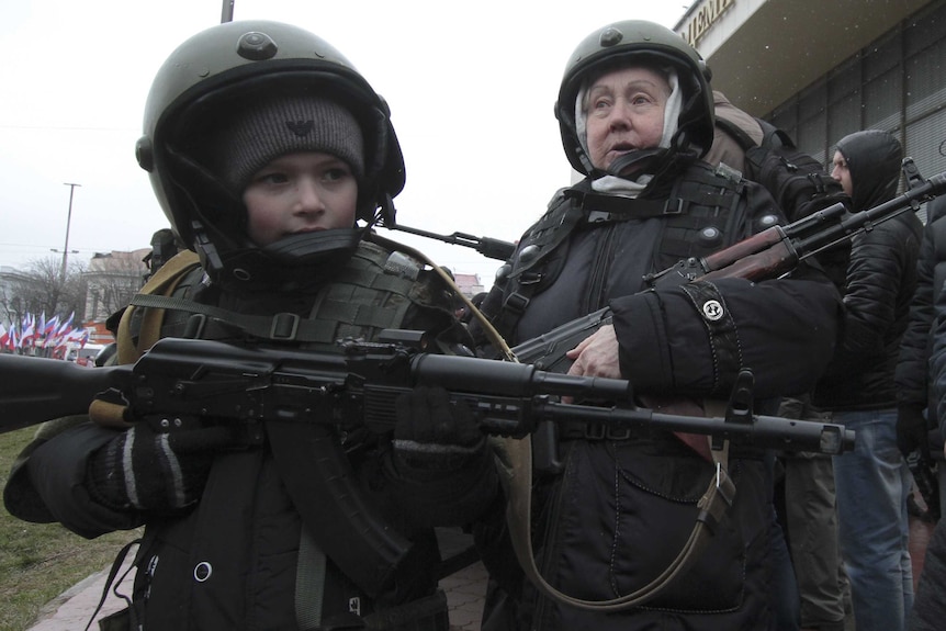 A boy and elderly woman pose with rifles during Defender of the Fatherland Day