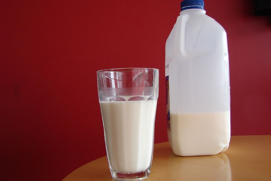 A two-litre bottle of milk sits on a table next to a glass of milk.