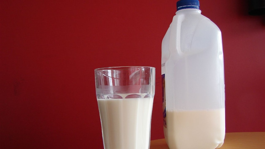 A two-litre bottle of milk sits on a table next to a glass of milk.