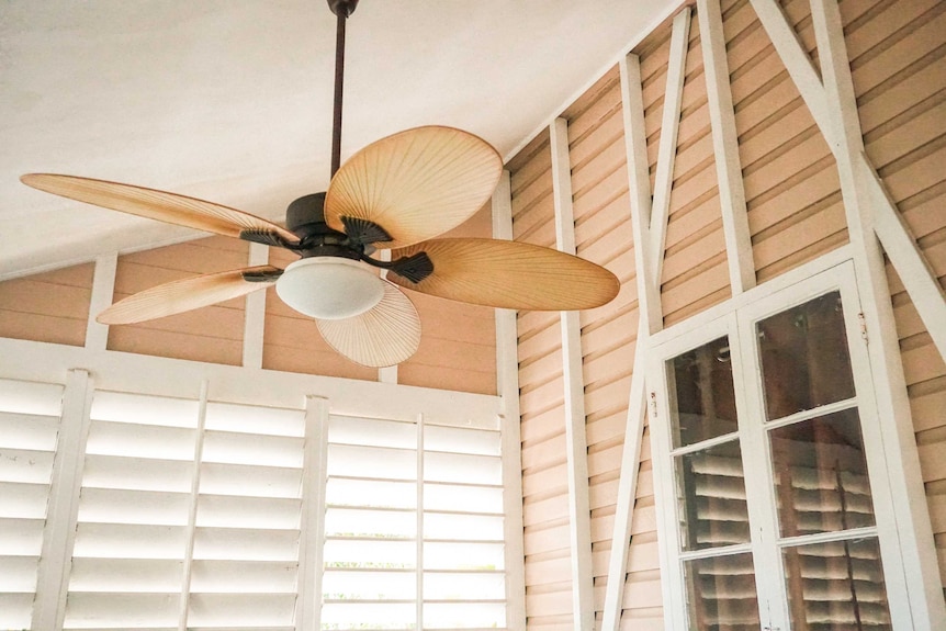 A ceiling fan in a house with shutters.