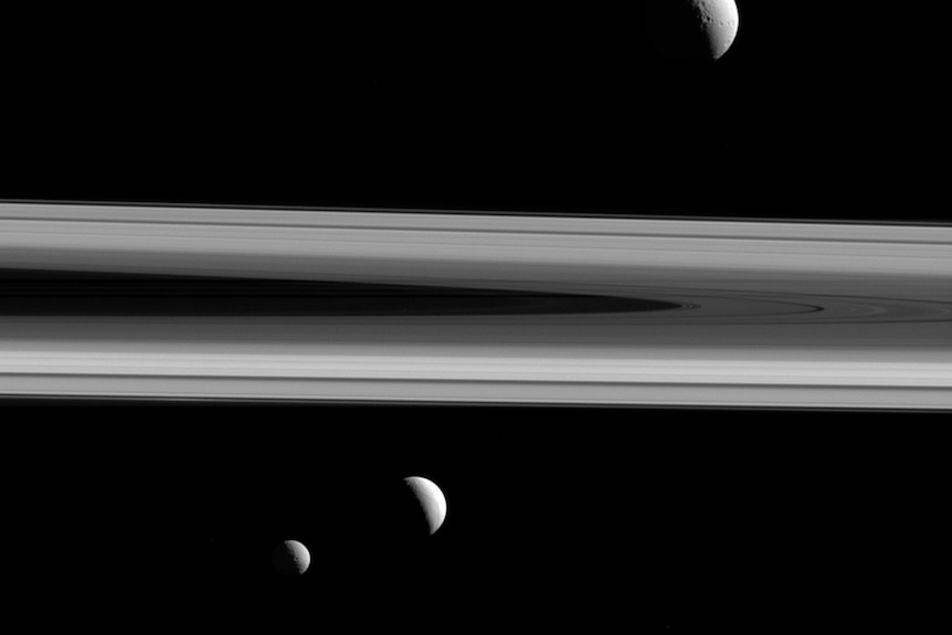 One of Saturn's rings is pictured with three differently sized half moons around it.