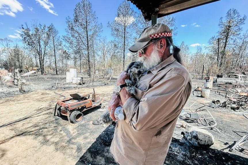 a man hold a dog in a bushfire affected property