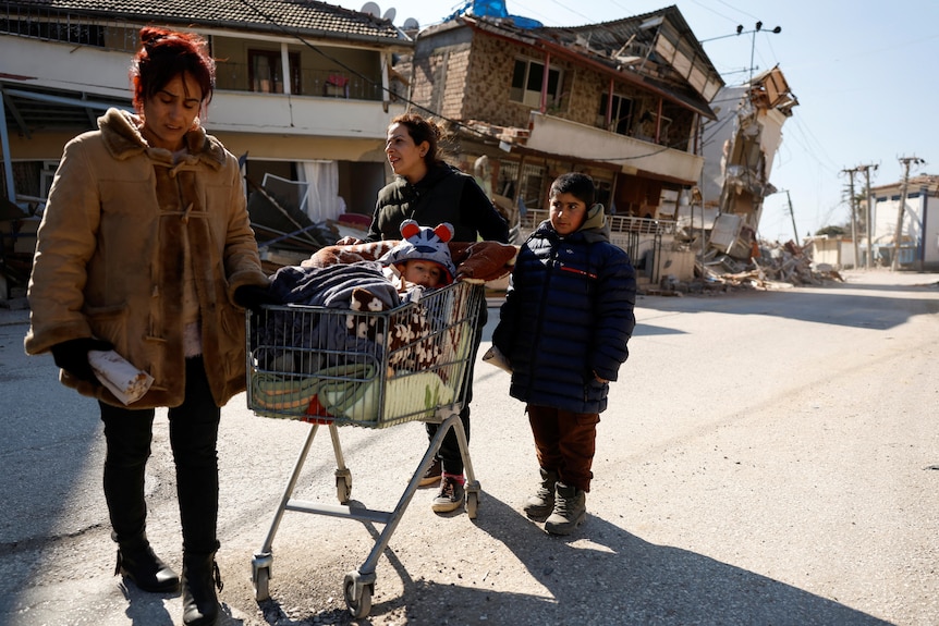 A family stand with a trolley in front of buildings that have been destroyed.  