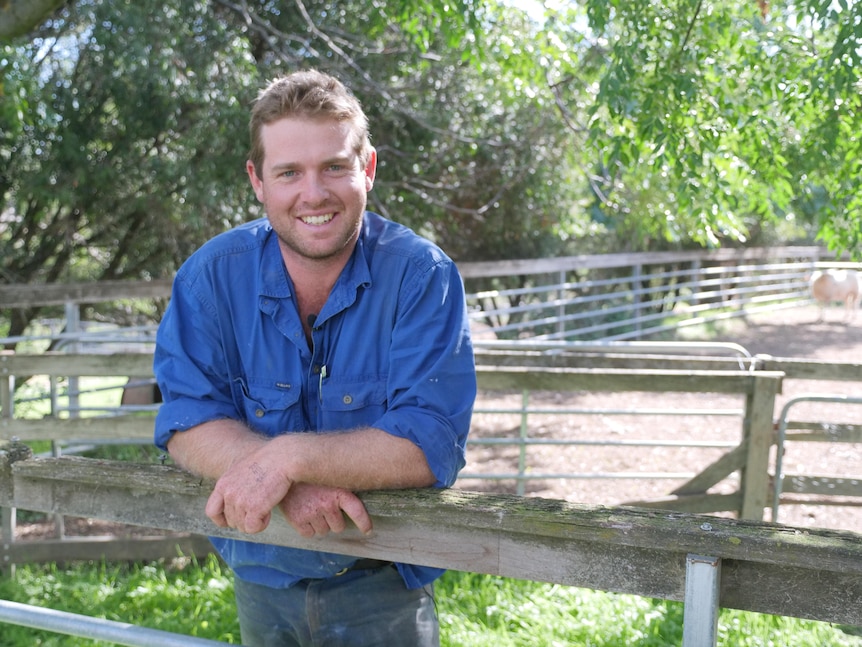 A man in a blue shirt leaning on a fence rail smiling. 