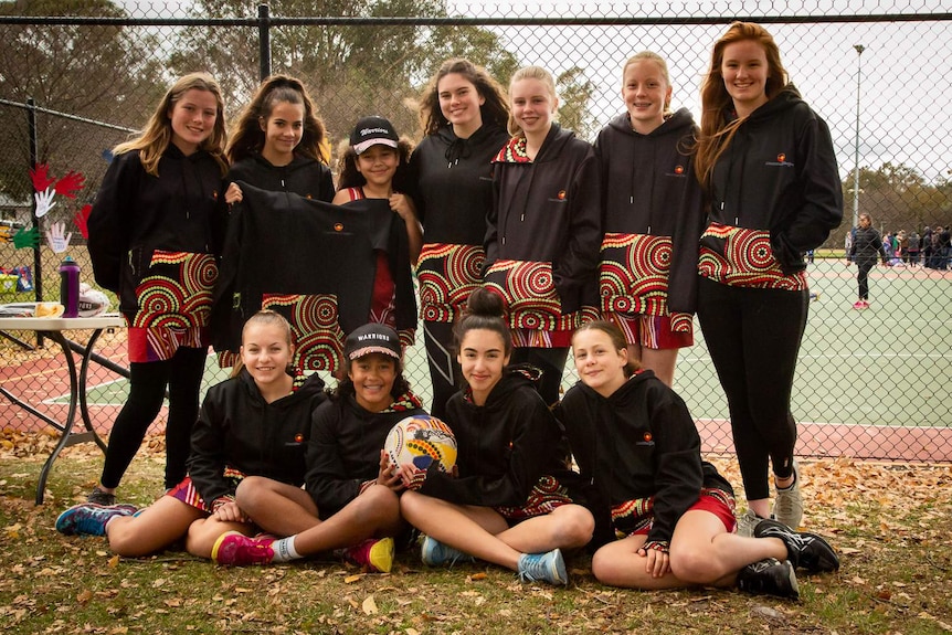 The Warriors netball team from Canberra are smiling together in a group.