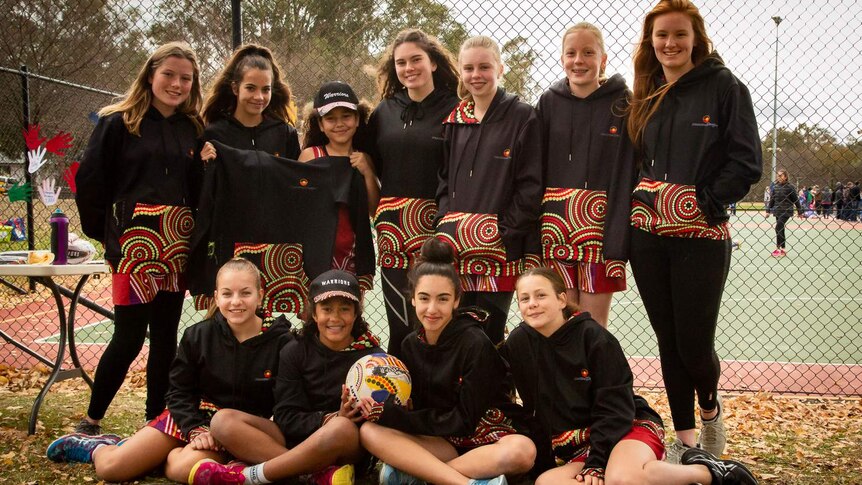 The Warriors netball team from Canberra are smiling together in a group.