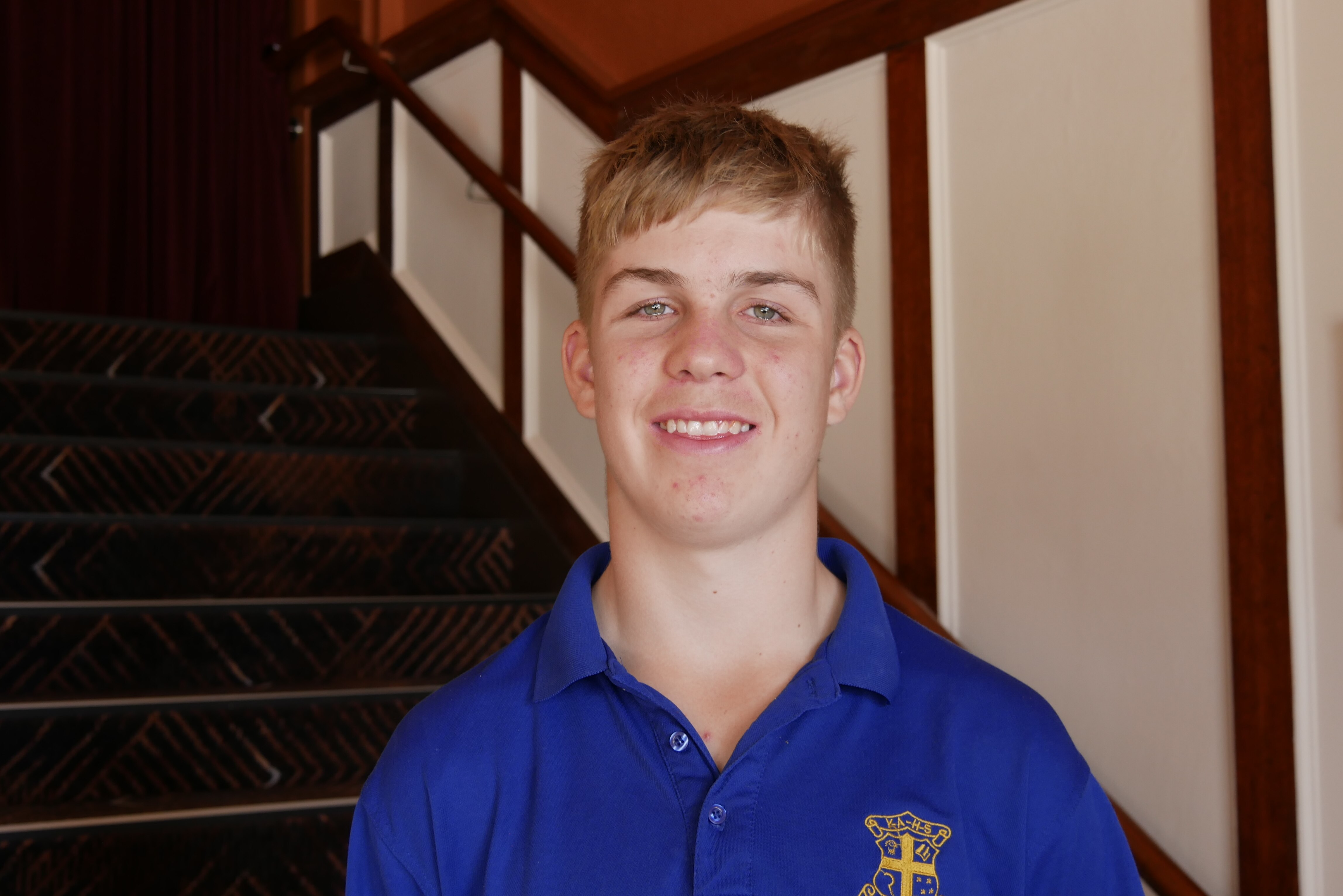 Teenage boy stands with blue top in front of a staircase
