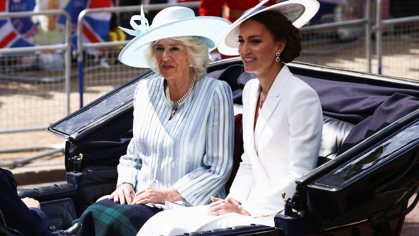 The Duchess of Cambridge and the Duchess of Cornwall ride in a carriage while wearing big hats.