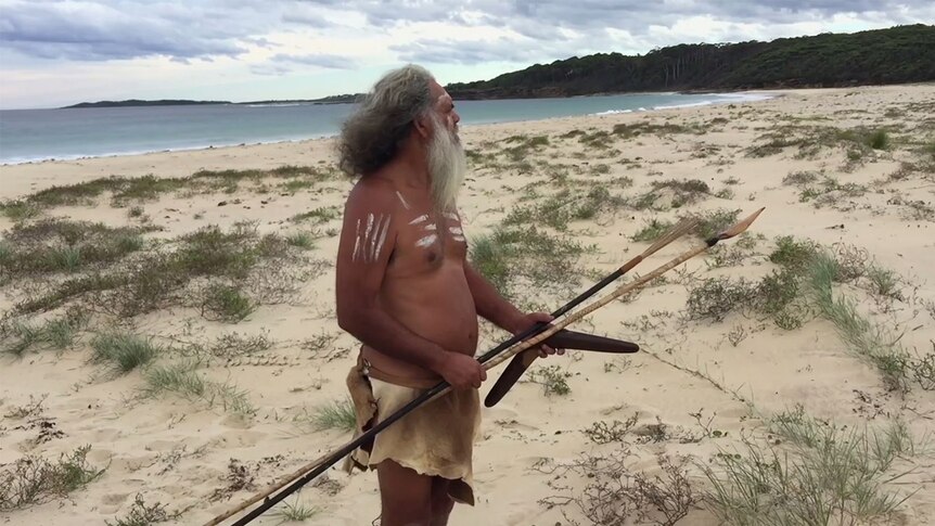 An Indigenous man stands on a beach