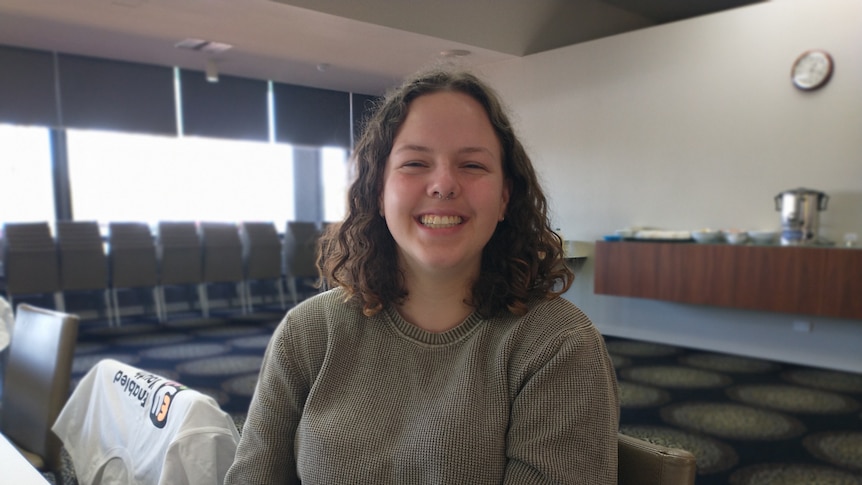 A young woman with curly hair smiling at the camera in a meeting room. 