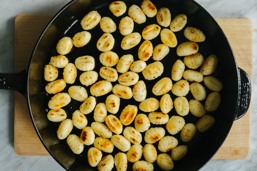 A cast iron pan with golden pan-fried gnocchi which has been cooked at high heat, ready to add to a salad.