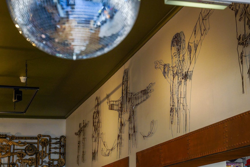A mirror disco ball hangs from a ceiling near black stencil-style artwork on a wall.