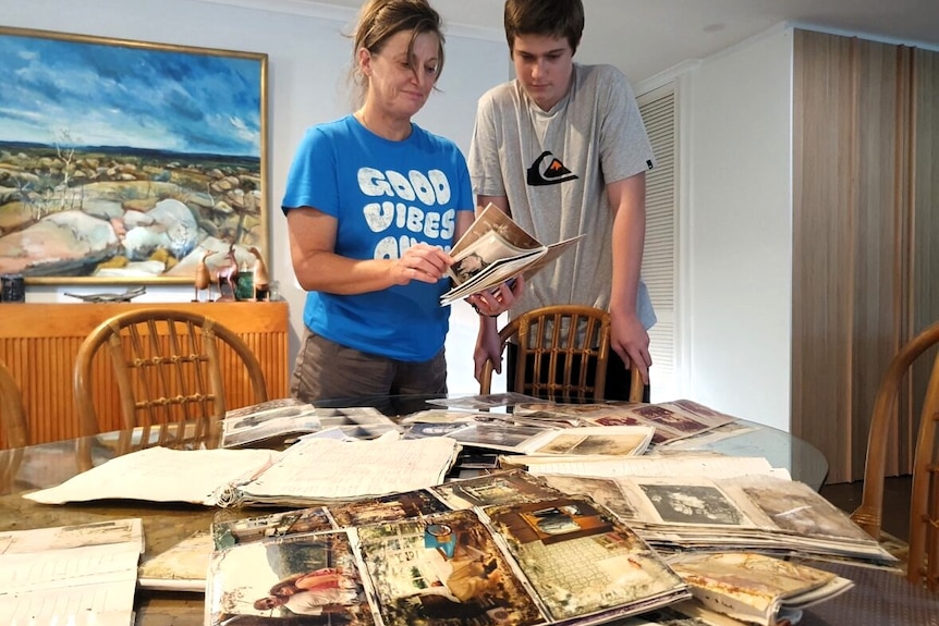 Woman and teenage boy looking at photo album with a table in front laden with photos.