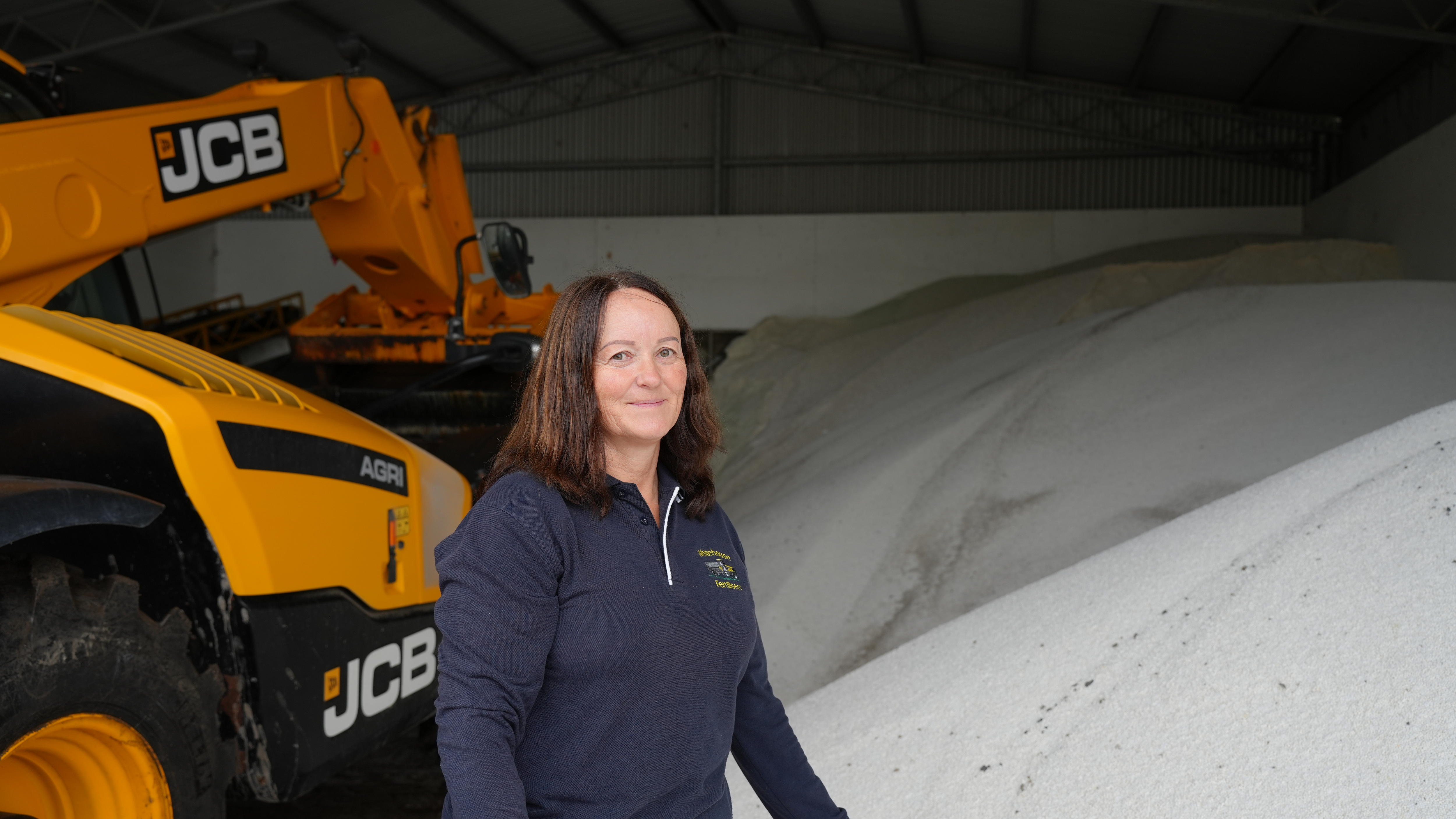 A woman on a farm stands next to a large heap of white fertiliser.