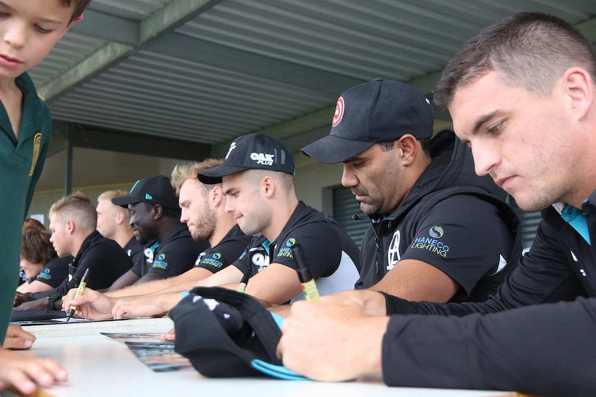 The Port Adelaide boys sit in a long line up, signing club merchandise for children