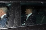 Prince Harry is pictured in the back of a black car. Rain droplets cover the window.