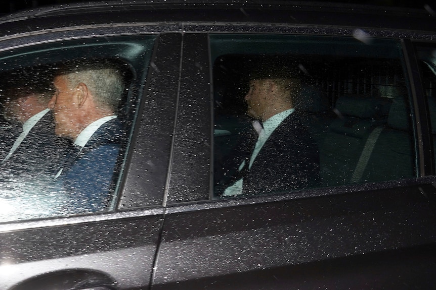 เจ้าชายแฮรี่นั่งเบาะหลังรถสีดำโดนฝน มีคนสองคนนั่งเบาะหน้า
