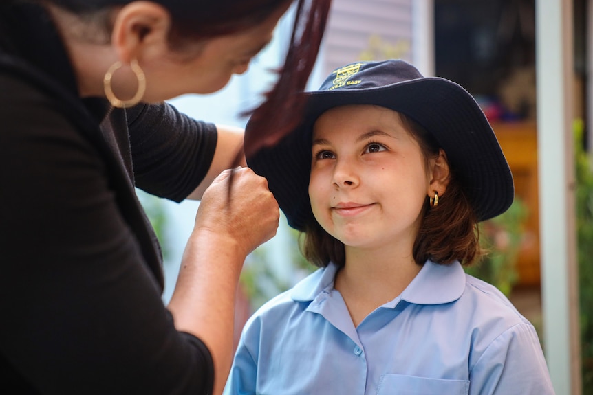a young girl looking at her mother as she puts on her hat
