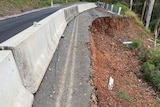 A section of a mountain road washed away, with large cracks across the remaining surface.