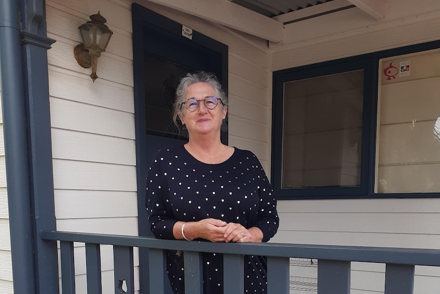 Woman standing on a front house porch smiling.