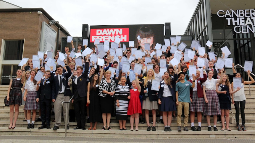 Students pose on the steps of the Canberra Theatre Centre, holding their certificates in the air.
