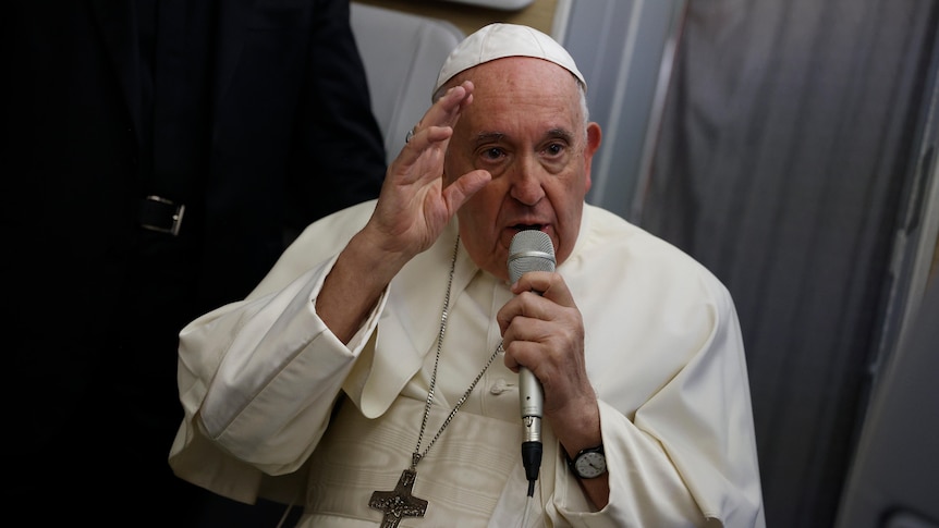 Pope Francis holding a microphone with one hand raised