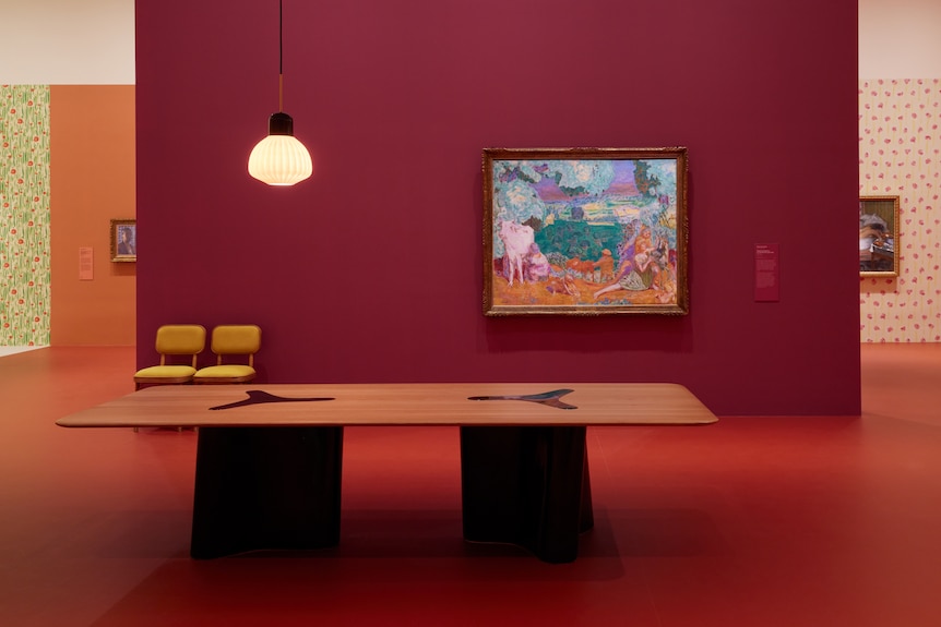 Installation view of gallery showing brightly painted walls hung with oil paintings, with a large table in foreground.