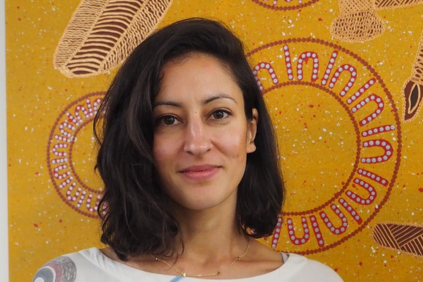 A portrait of Stephanie Tonkin, which an Indigenous art work in the background.