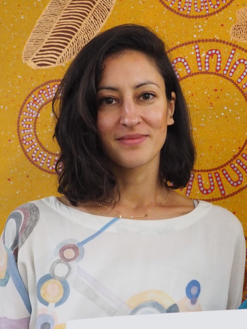 A portrait of Stephanie Tonkin, which an Indigenous art work in the background.