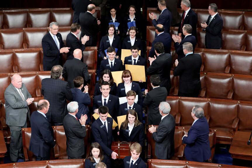 People holding manila envelopes walk through the US House of Representatives while men in suits applaud them