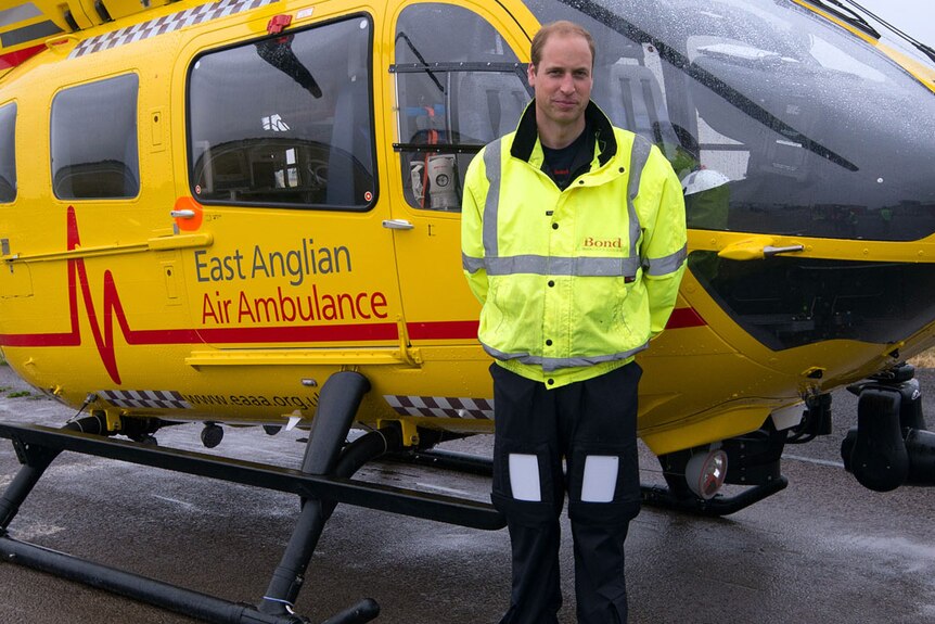 Prince William in a bight yellow high-visibility jacket in front of a yellow helicopter 