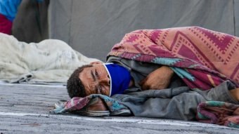 A man lies on the ground wrapped in a blanket with a blue facemask.