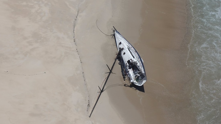 A top-down shot shows a yacht on a beach with its mast askew.