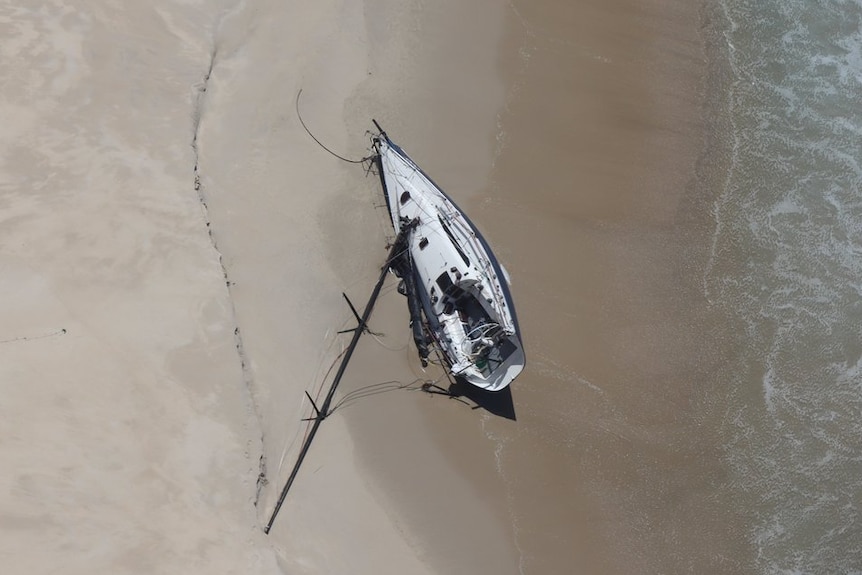A top-down shot shows a yacht on a beach with its mast askew.