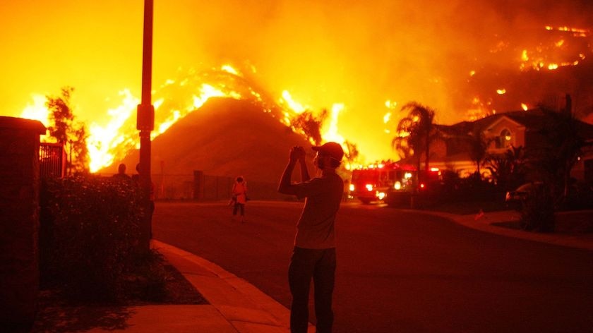 A resident takes photos as fire comes close to homes in Yorba Linda, California