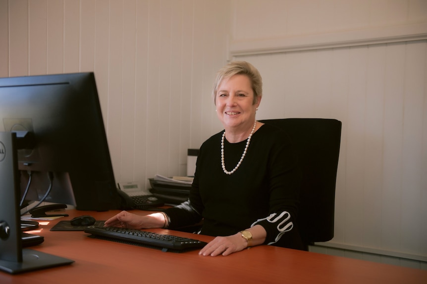 A woman in black sits at her desk.