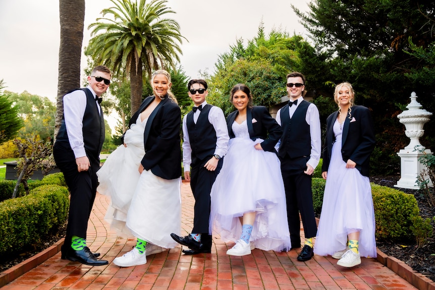 Six young people in formal attire, showing off sneakers and bright sock.
