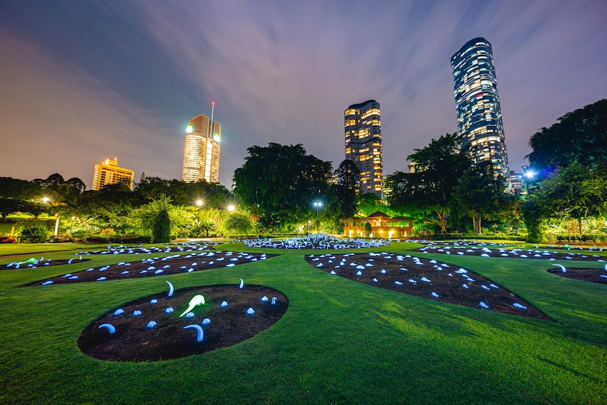 Art installation lit up in the evening with Brisbane city buildings in the background.