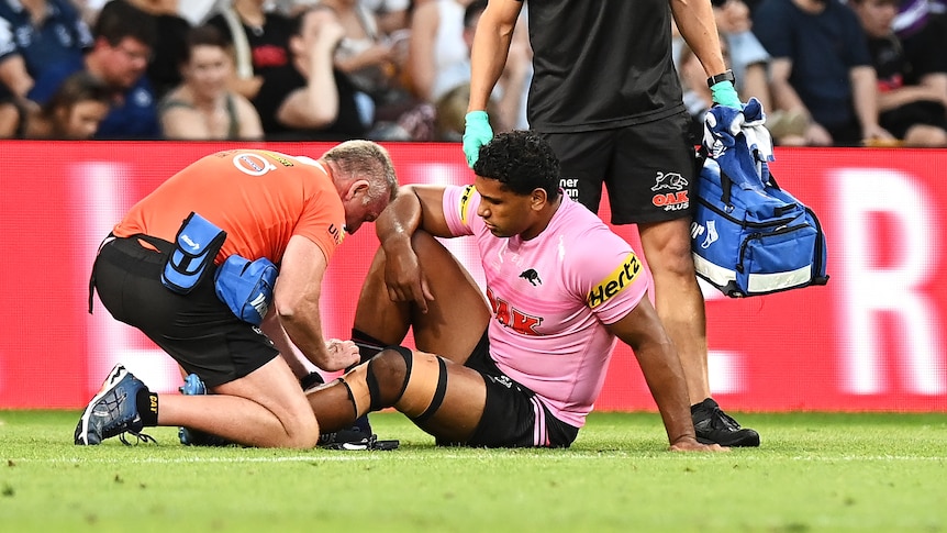 A Penrith Panthers NRL player receives treatment on an injured knee during a match against the Melbourne Storm.