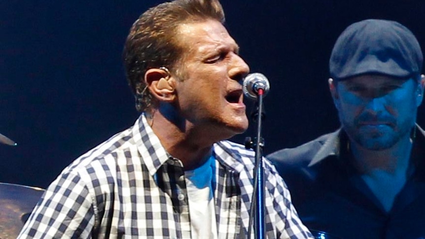 Glenn Frey plays guitar onstage with The Eagles, their drummer behind him.