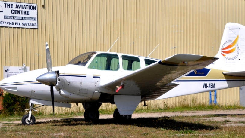A twin-engine plane sits in front of an airplane hangar.
