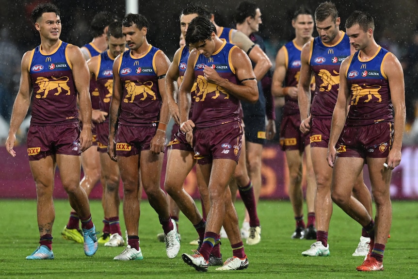 A group of dejected Brisbane Lions AFL players walk off the ground with their heads down.